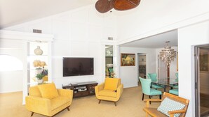 A spacious living room with a flat-screen TV, yellow sofas, a glass dining table with teal chairs, and a chandelier. - 3-bedroom Jupiter condo in gated community (Jupiter)