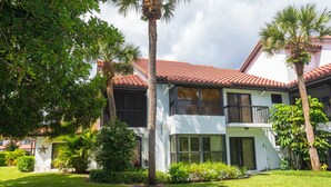 A two-story house with a red-tiled roof, large windows, and a well-maintained lawn with palm trees. - 3-bedroom Jupiter condo in gated community (Jupiter)