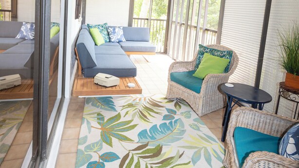A sunlit patio with a sofa, a wicker chair, and a small table. - 3-bedroom Jupiter condo in gated community (Jupiter)