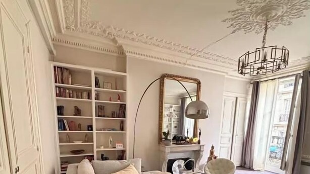 Ein modernes Wohnzimmer mit einem beigefarbenen Ecksofa, einem großen Spiegel und einem Bücherregal.