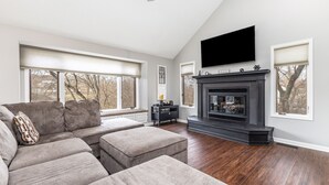 A living room with a sectional sofa, a fireplace, and a flat-screen TV mounted above it. - 3BdRoom Home w/ Hot Tub + Game Room (Galena)