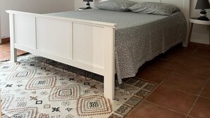 A bedroom with a white bed, patterned rug, and a sun-shaped wall decoration. - Apartment with sea and pool view (Le Gosier)
