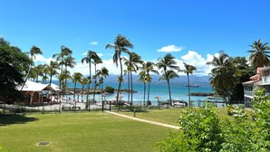 A beachfront view with palm trees, a pool area, and a clear blue sky. - Apartment with sea and pool view (Le Gosier)
