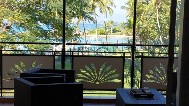 A balcony with a view of a pool and palm trees, featuring black outdoor furniture and a decorative plant design on the railing. - Apartment with sea and pool view (Le Gosier)