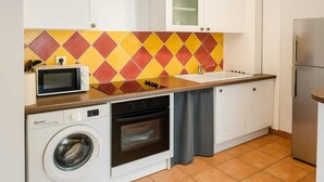A compact kitchen with a washing machine, microwave, oven, and a sink with a tiled backsplash. - Apartment with sea and pool view (Le Gosier)