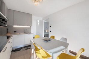 Eine moderne Küche mit weißen Schränken, einer zentralen Kochinsel und einem Essbereich mit weißem Tisch und gelben Stühlen.
