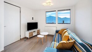 Een moderne woonkamer met een bank, een televisie, een kleine tafel en een raam met uitzicht op bergen.