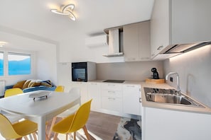 Une cuisine moderne avec des meubles blancs, un évier en acier inoxydable et un coin repas comprenant une table blanche et des chaises jaunes.