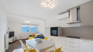 Een moderne keuken met witte kasten, een ingebouwde oven en een eethoek met een witte tafel en gele stoelen.