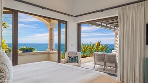 Een slaapkamer met een groot bed, een aan de muur bevestigde televisie en een balkon met uitzicht op de oceaan.