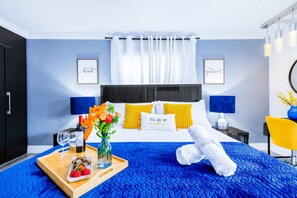 Habitación de hotel con cama, bandeja de comida y bebidas, un florero con flores y dos marcos con citas motivacionales en la pared.