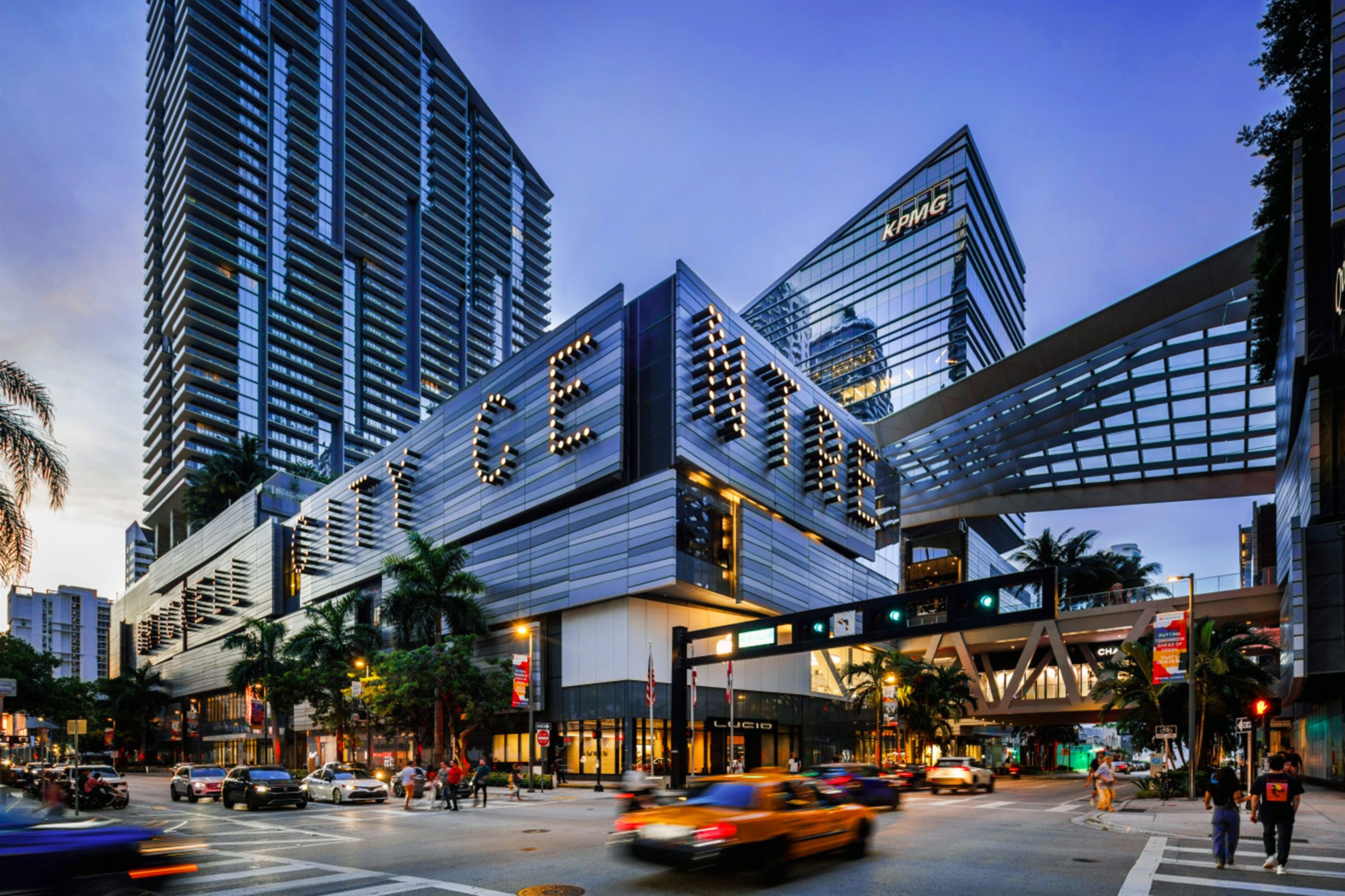 A modern building with a prominent sign, surrounded by high-rise buildings and busy traffic.