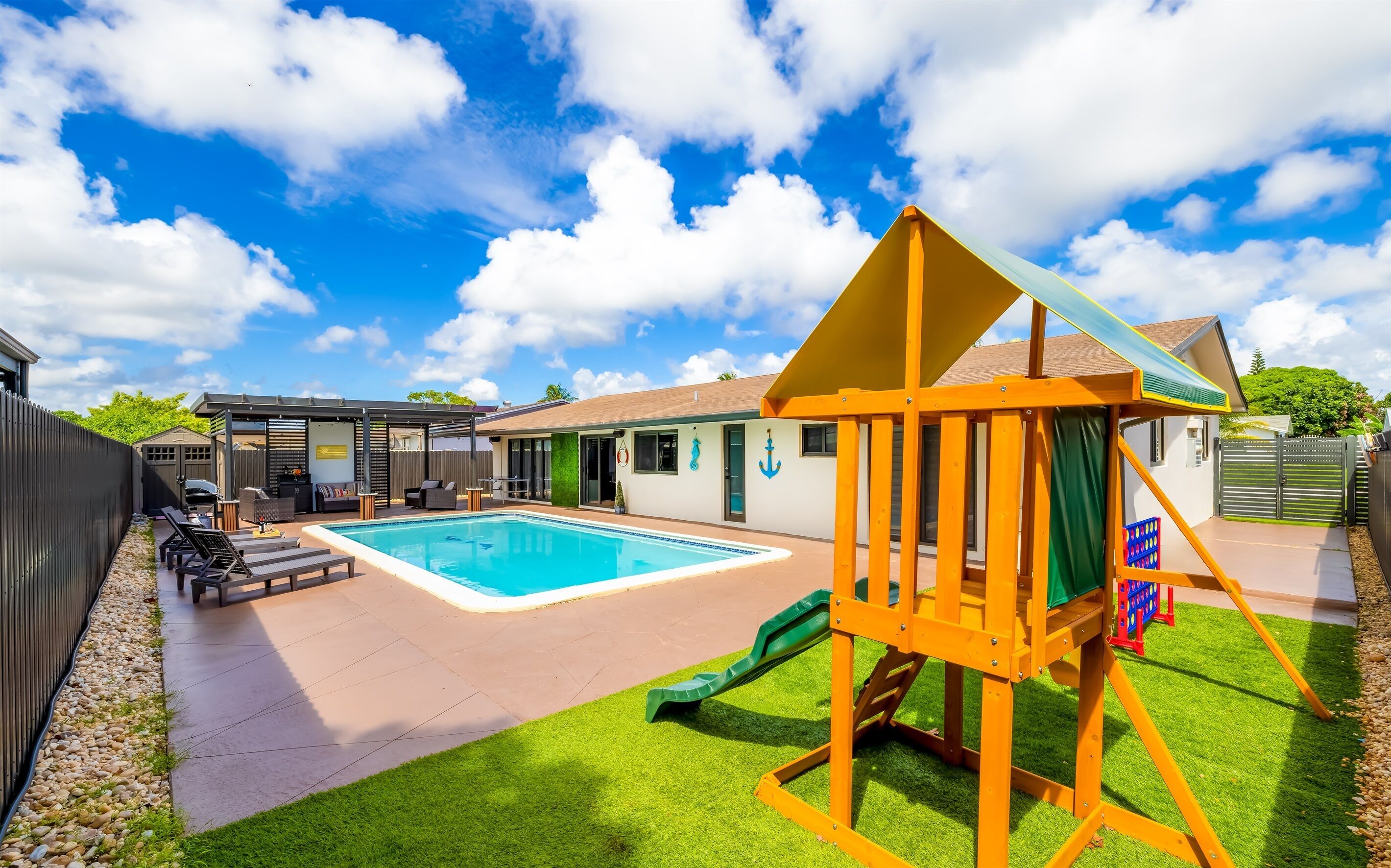 Un jardin avec une piscine, une aire de jeux pour enfants et un espace détente couvert.