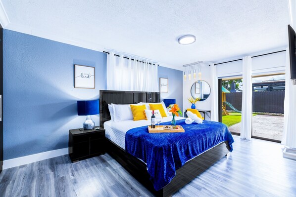 Un dormitorio con cama, mesitas de noche, una mesilla auxiliar, una bandeja con objetos y vistas al exterior.