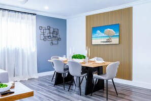 Un comedor moderno con una mesa de madera, sillas grises, un adorno en la pared y una escena de playa enmarcada.