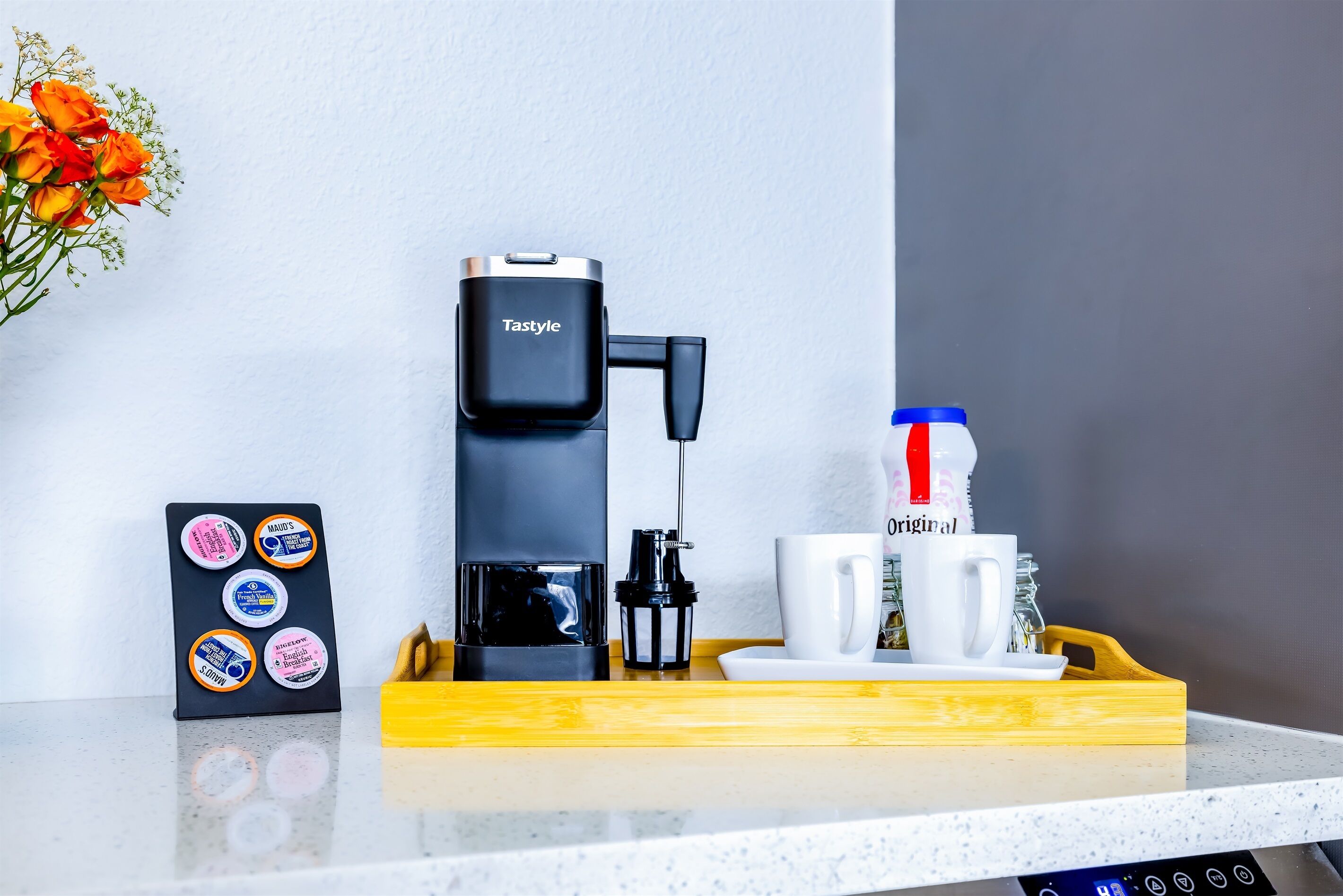 A coffee maker, a mug, a tray, and a card with coffee pod labels on a countertop.