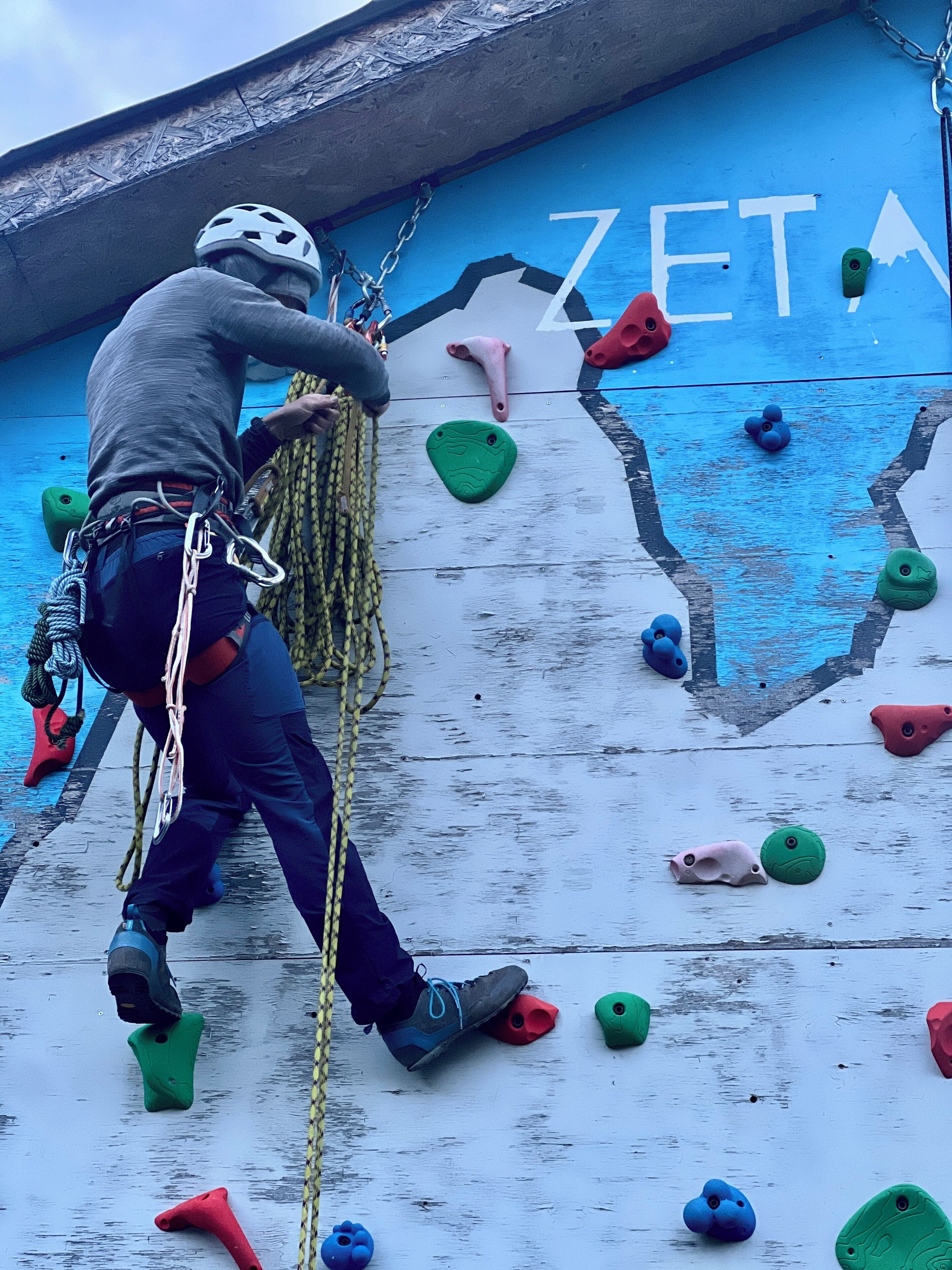 A person climbing a wall with climbing holds and a rope.