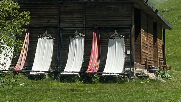 A wooden cabin with a sloped roof, set against a backdrop of a mountain with snow patches. - Zeta Camping (Juta)