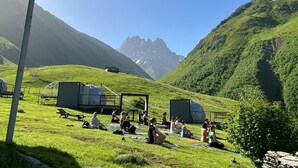 A group of people meditating in a grassy field with tents and a mountain in the background. - Zeta Camping (Juta)