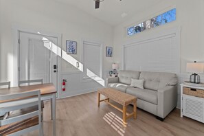 A modern living room with a sofa, a bench, a dining table, and a staircase. - Cozy Coastal Cottage #61 (North Myrtle Beach)