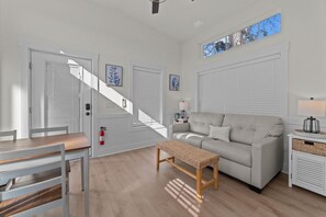 A modern living room with a sofa, a bench, a dining table, and a staircase leading to another level. - Cozy Coastal Cottage #63 (North Myrtle Beach)