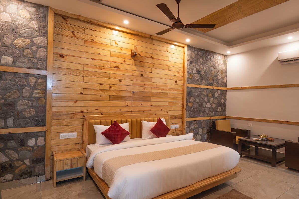 A bedroom with a wooden headboard, a bed with white and red bedding, a nightstand, a small table with a lamp, and a ceiling fan.