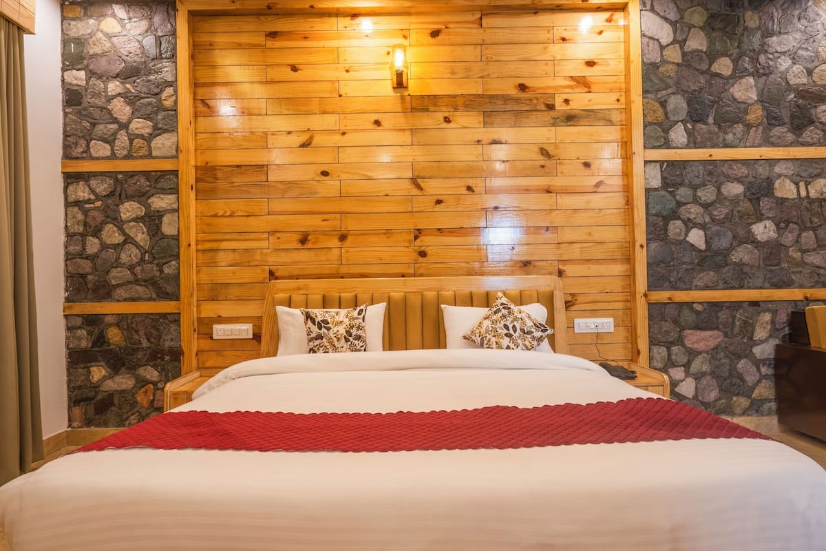A bed with a wooden headboard, stone walls, and a red throw blanket.