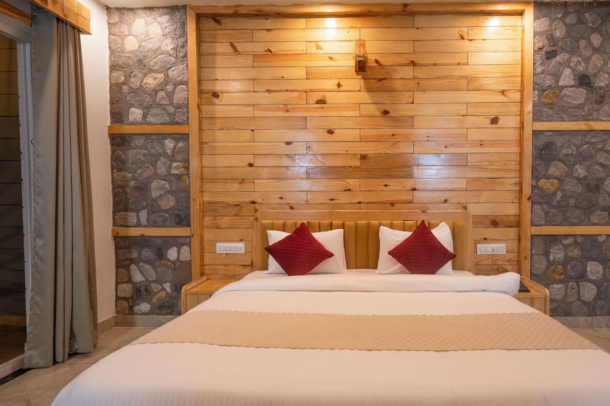 A bedroom with a wooden headboard, stone walls, and a bed with white and red pillows.