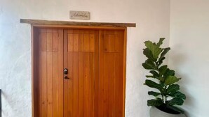 A wooden door with a sign above it, a potted plant beside it, and a tiled floor. - Casa Monica - Apt Astromelia (Barichara)