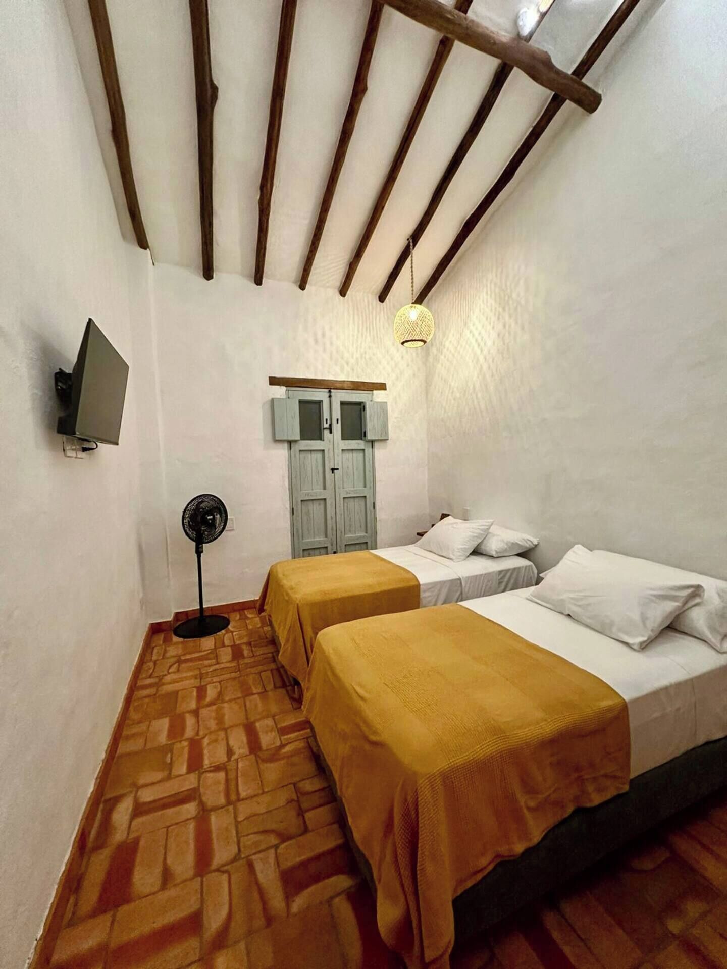 Een kleine, knusse kamer met twee bedden, een ventilator, een televisie en een hanglamp.
