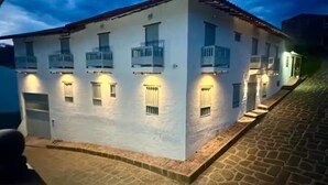 A two-story building with a white facade and a red-tiled roof. It features multiple balconies and windows with external lighting. - Casa Monica - Apt Astromelia (Barichara)