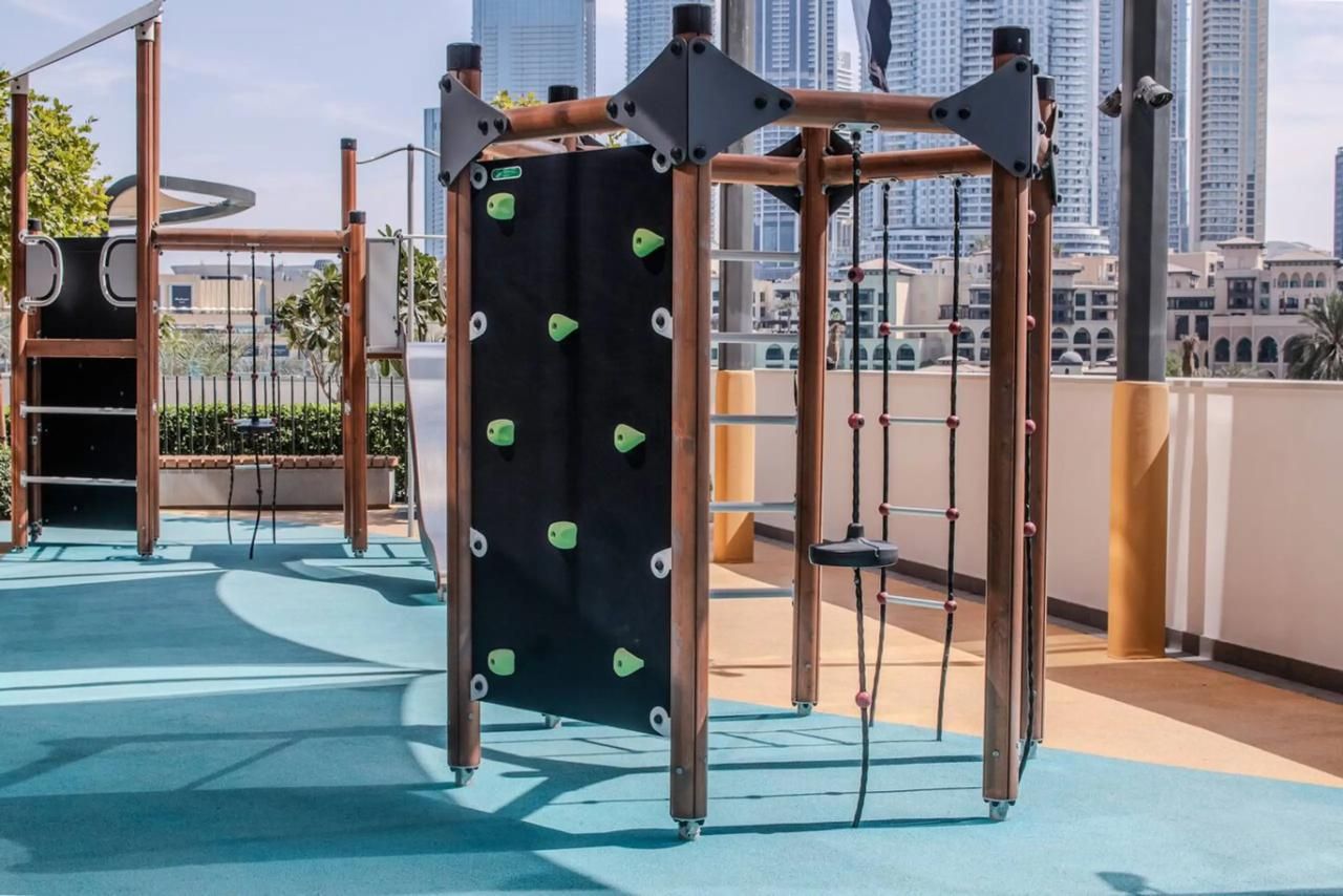 A rooftop playground with climbing structures and swings, surrounded by a cityscape.