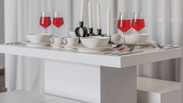 A white table with red wine glasses, white candles, and silverware.