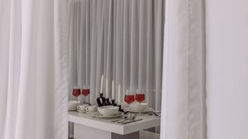 A dining table set with white tableware and red wine glasses, with candles and a white curtain in the background.