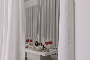 A dining table set with white tableware and red wine glasses, with candles and a white curtain in the background. - Elegant Stay with Burj Khalifa View (Dubai)
