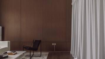 A modern living room with a dark wood panel wall, a black chair, a white sofa, and a white curtain.
