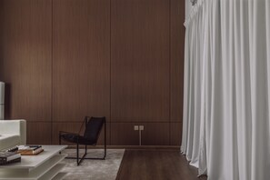 A modern living room with a dark wood panel wall, a black chair, a white sofa, and a white curtain. - Elegant Stay with Burj Khalifa View (Dubai)