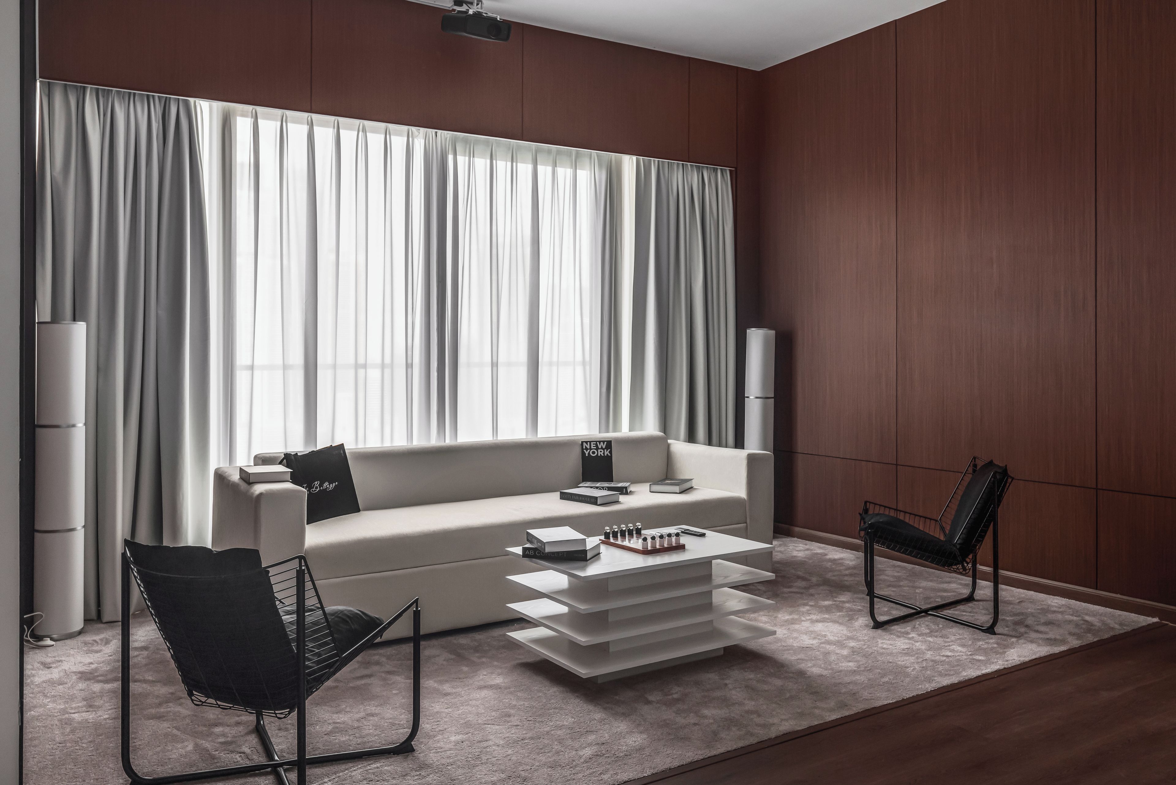 Ein modernes Wohnzimmer mit einer Couch, zwei Sesseln, einem Couchtisch und einem großen Fenster mit Vorhängen.