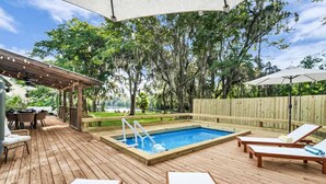 Eine Holzterrasse mit Swimmingpool, Liegestühlen und einer überdachten Sitzecke.