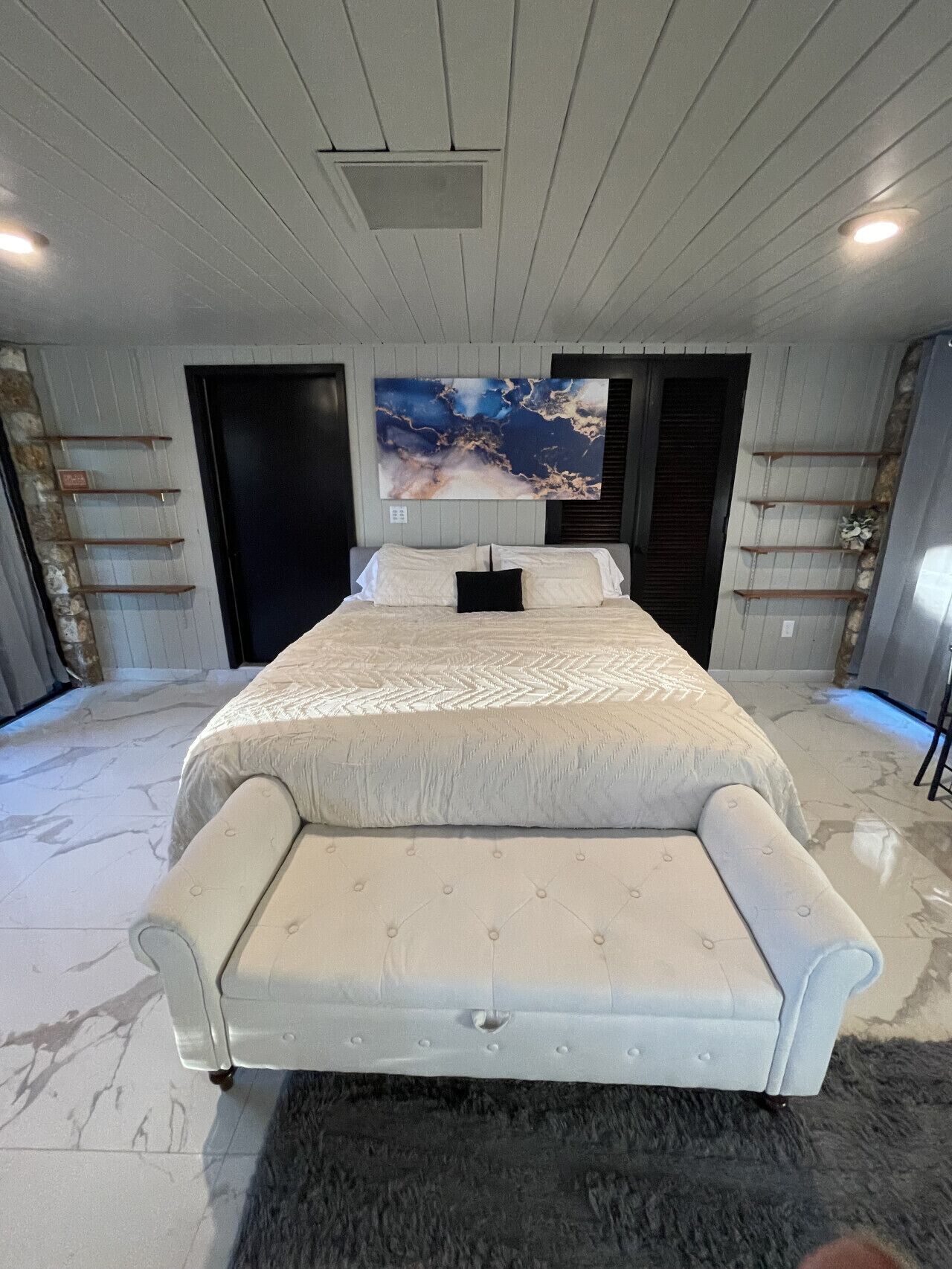 A bedroom with a large bed, a headboard, a wall-mounted painting, and a ceiling light.