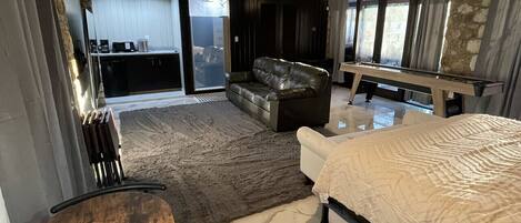 Een moderne slaapkamer met een groot bed, een houten stoel, een bank en uitzicht op een keuken en balkon.