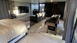 A modern bedroom with a large bed, a foosball table, and a seating area with a TV.