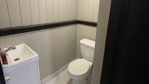 A small, compact bathroom with white walls, a white toilet, and a white sink.