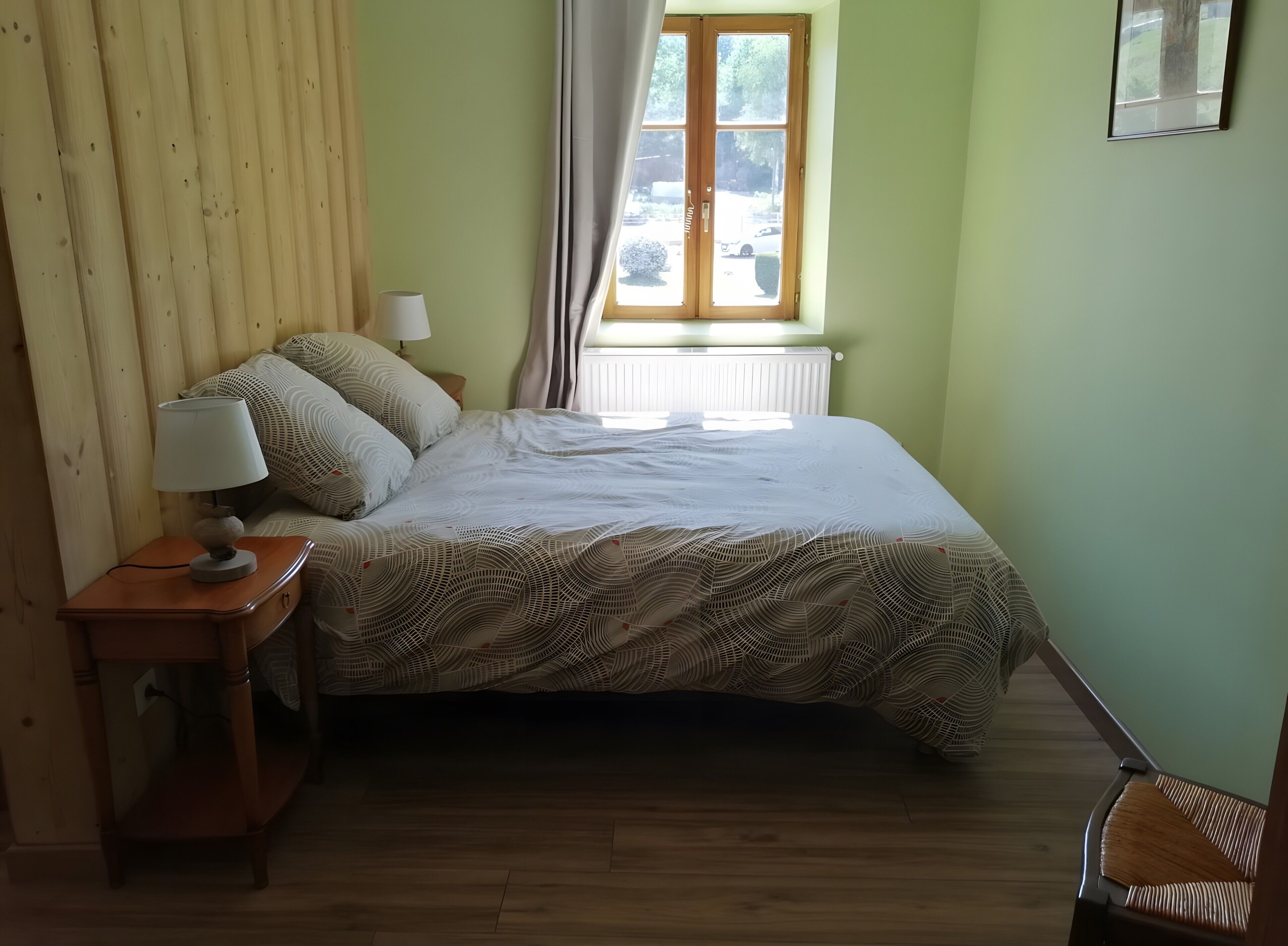 Een slaapkamer met een bed, nachtkastje, lamp, raam met gordijnen en een radiator.
