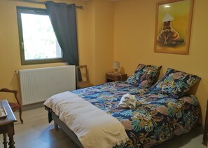 A bedroom with a bed, a chair, a table, a window with curtains, a radiator, a nightstand with a lamp, and a painting on the wall. - Room 'La Mirabelle' with Shared Terrace, Wi-Fi and Air Conditioning (Rehaupal)