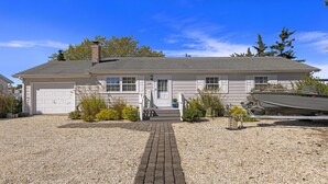 A single-story house with a front garage, a welcoming entrance, and a gravel driveway. - Lagoonfront Home in Beach Haven West with a pool & kayaks! (Manahawkin)