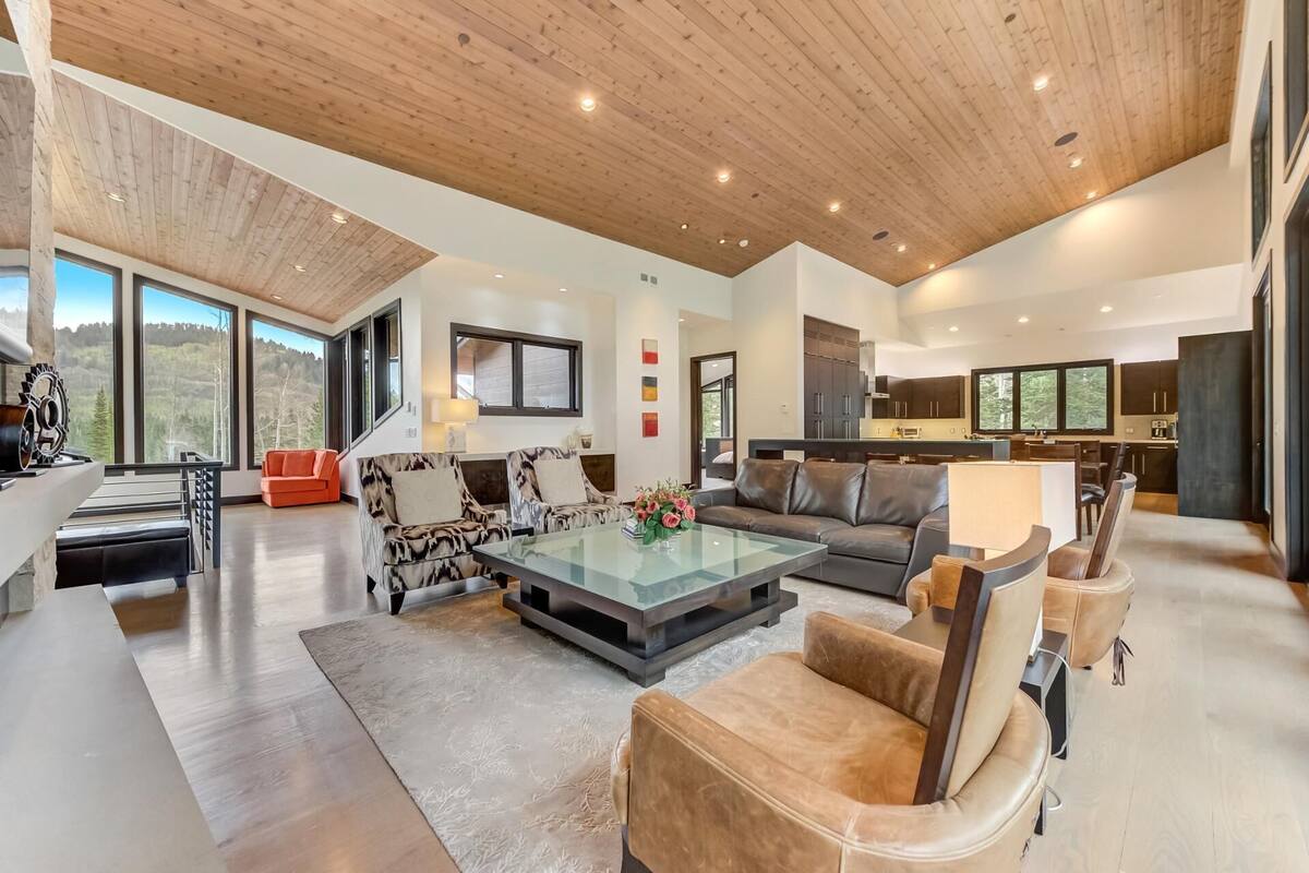 A spacious living area with a high ceiling, large windows, and a modern kitchen.
