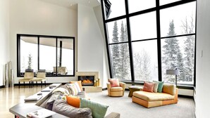 A spacious living room with a fireplace, large windows, and a view of snow-covered trees. - The Colony at White Pine Canyon by KBM (Park City)