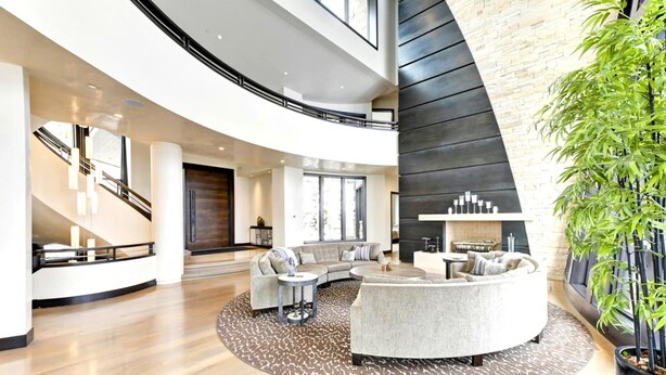 A spacious living area with a curved sofa, a coffee table, and a fireplace. There is a staircase with a railing leading to an upper level. - The Colony at White Pine Canyon by KBM (Park City)