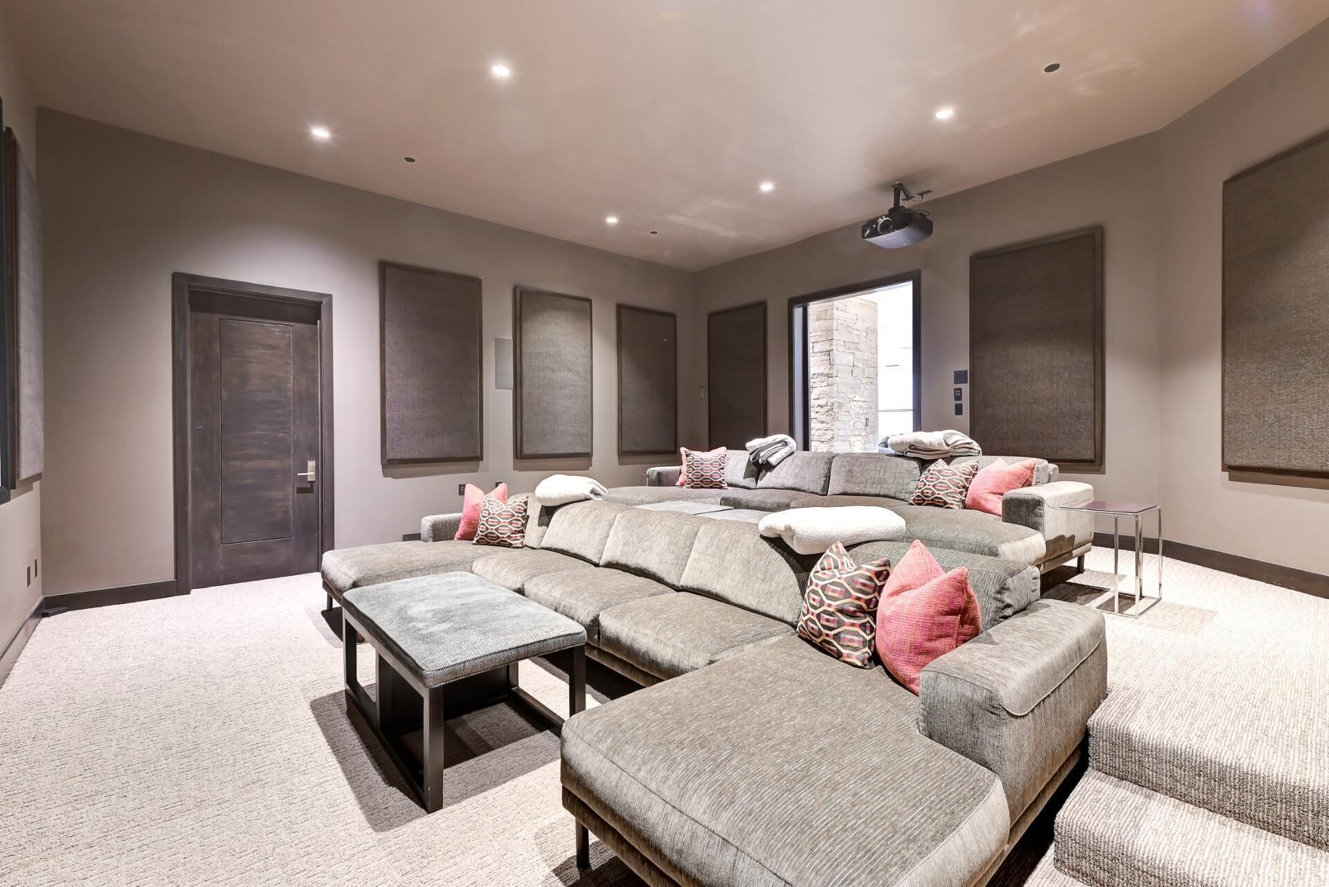 A home theater room with a sectional sofa, a small table, and a projector.